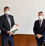 Person hält ein Dokument und steht neben einer Person