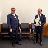 Eine Person hält ein Dokument und steht neben einer anderen
