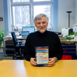 Person sitzt auf einem Schreibtisch und hält ein Buch