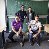 Vier Personen stehen in einem Raum vor der Tafel