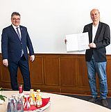 Person hält eine Bescheinigung in der Hand und steht neben einer anderen Person