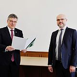 Eine Person hält ein Dokument in der Hand und steht neben einer Person