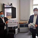 Zwei Personen tragen Masken und stehen voneinander entfernt
