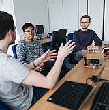 Drei Personen an einem Tisch unterhalten sich über etwas