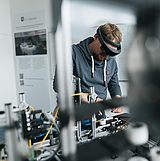 Person mit Brille arbeitet an einer Maschine